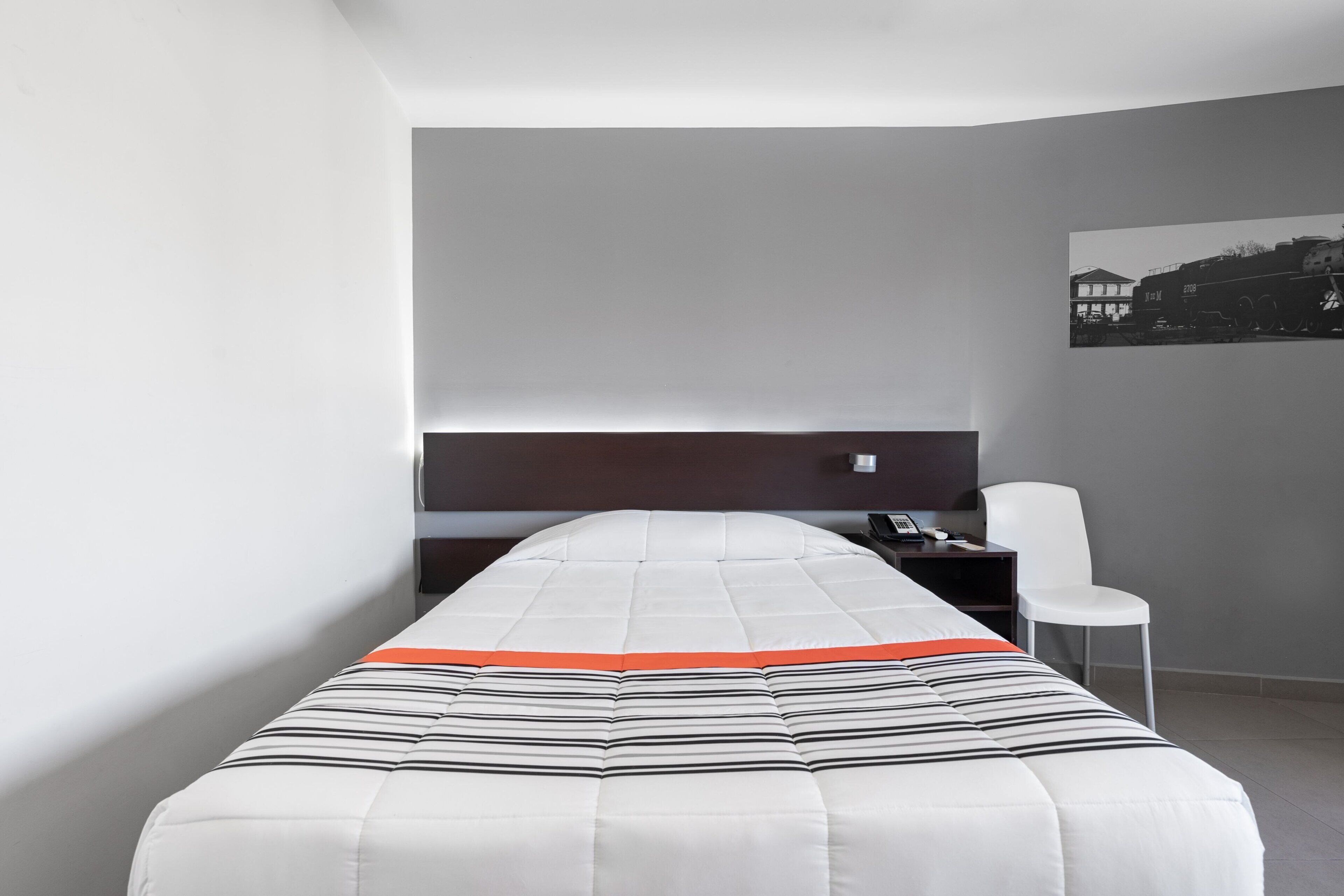 Habitación de hotel con una cama individual, un escritorio, una silla y un televisor montado en la pared.