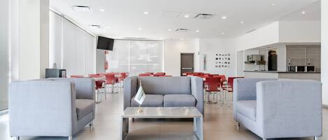 A spacious lobby with grey sofas, a coffee table, and red chairs.