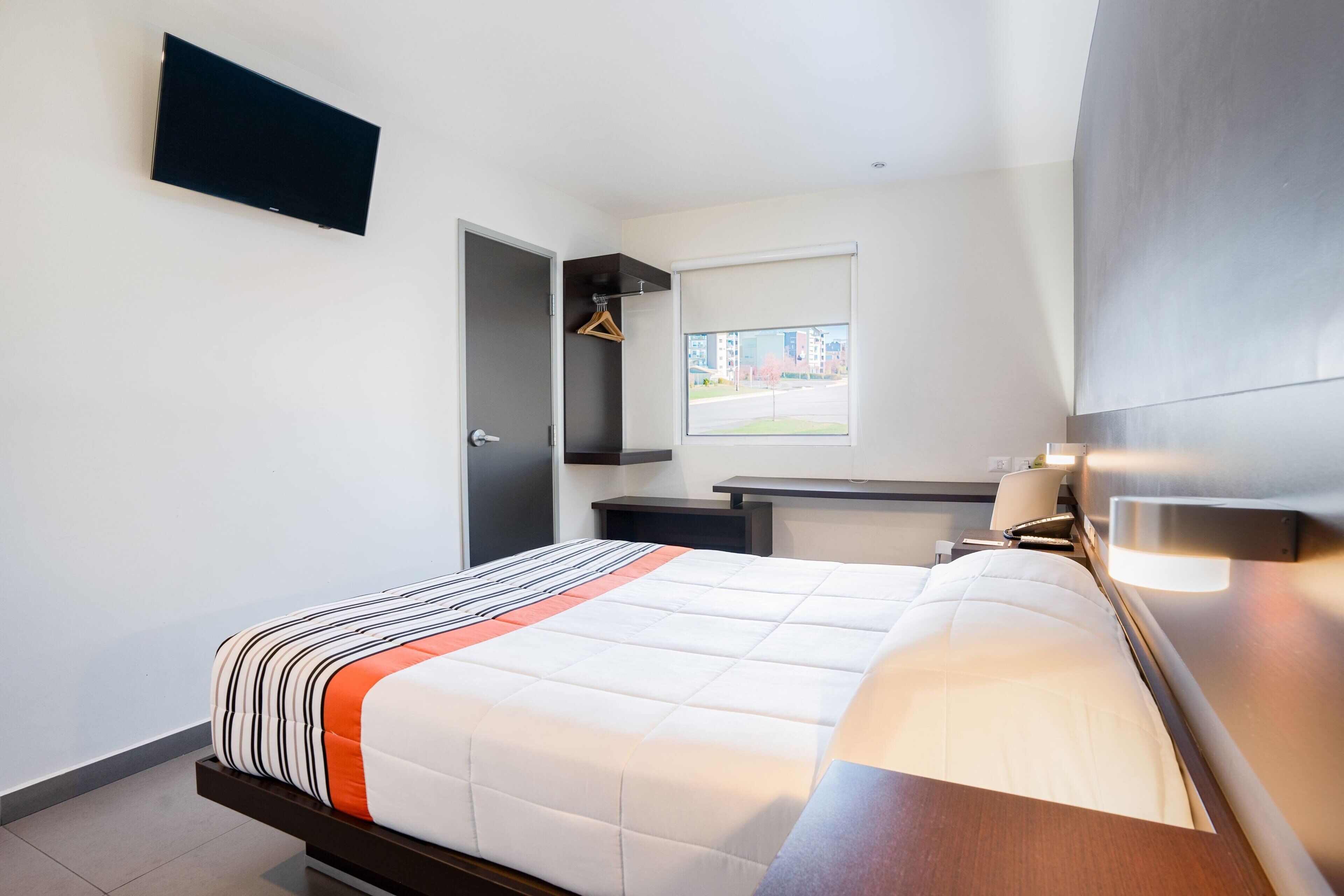 A modern hotel room with a bed, bedside table, and a flat-screen TV mounted on the wall.