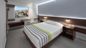A modern hotel room with a large bed, a desk, a chair, and a view of the city. - City Express Junior by Marriott Aguascalientes Centro (Aguascalientes)