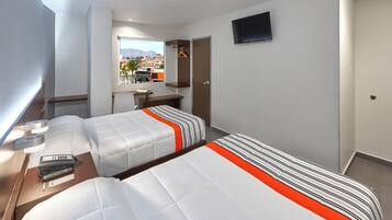 A hotel room with two beds, a desk, a chair, a TV, and a window with a city view.