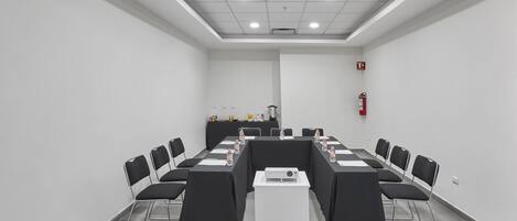 Un salón de conferencias con una larga mesa, sillas, un proyector y un extintor.