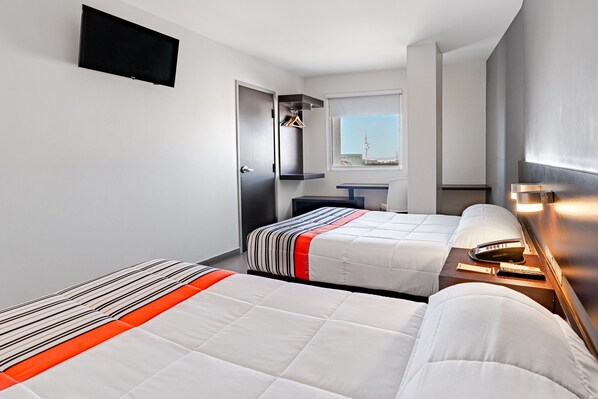 Une chambre d’hôtel avec deux lits, un téléviseur à écran plat, un petit bureau avec une lampe et une fenêtre donnant sur une tour.