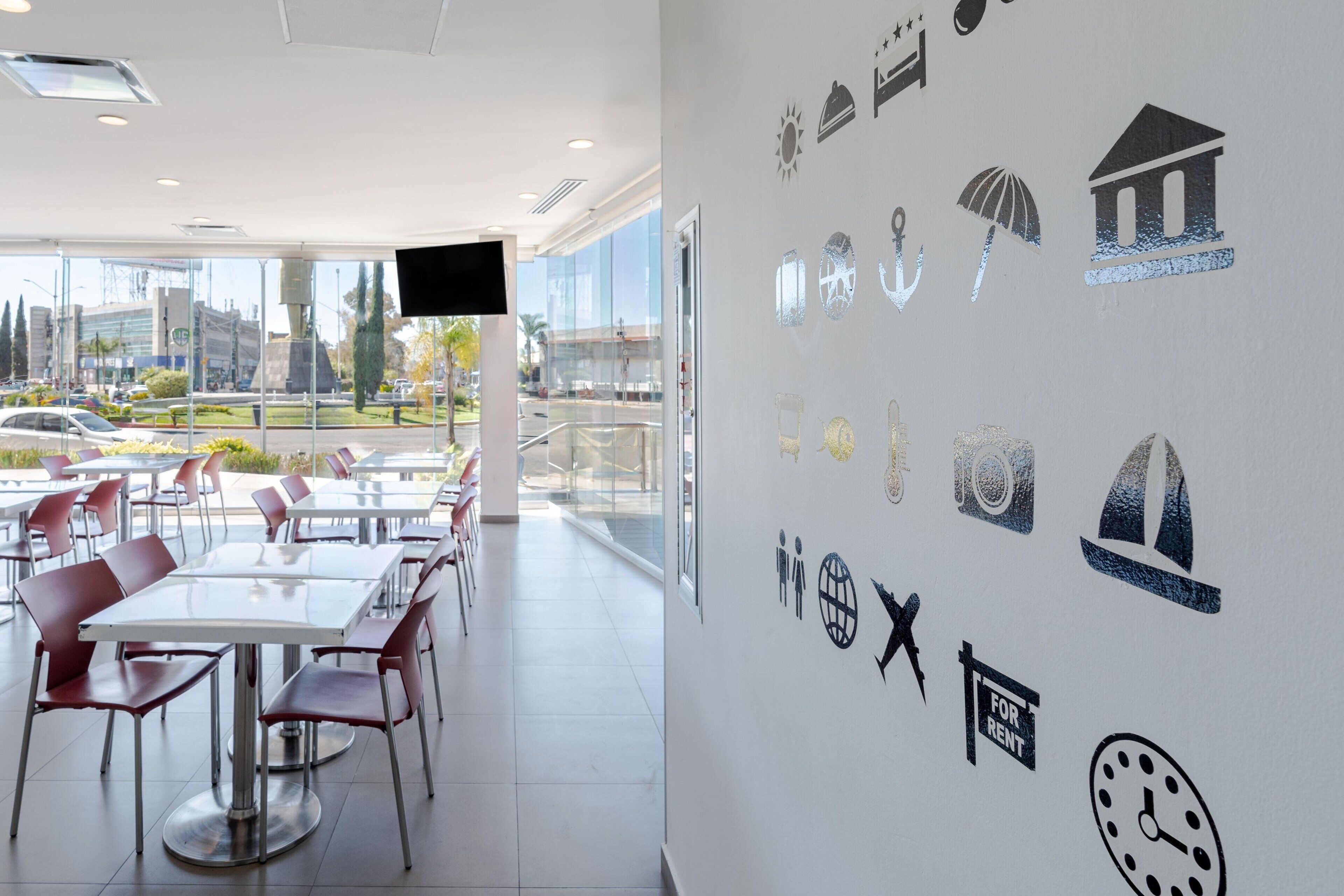 Un comedor moderno con mesas y sillas, un ventanal con vistas a la ciudad y una pared decorada con varios iconos.