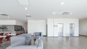 A spacious lobby with grey sofas, a coffee table, and a kitchen area in the background. - City Express Junior by Marriott Aguascalientes Centro (Aguascalientes)
