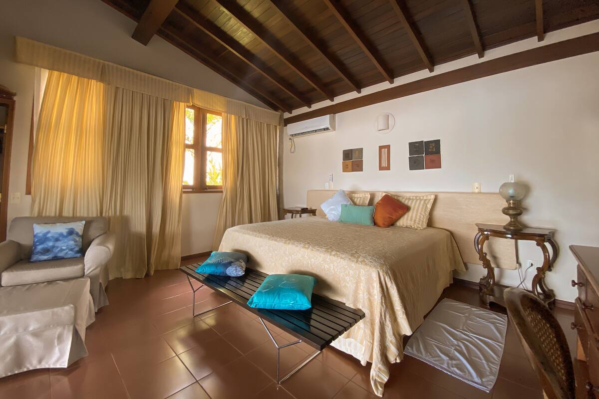 A bedroom with a bed, a chair, a table, and a window with curtains.
