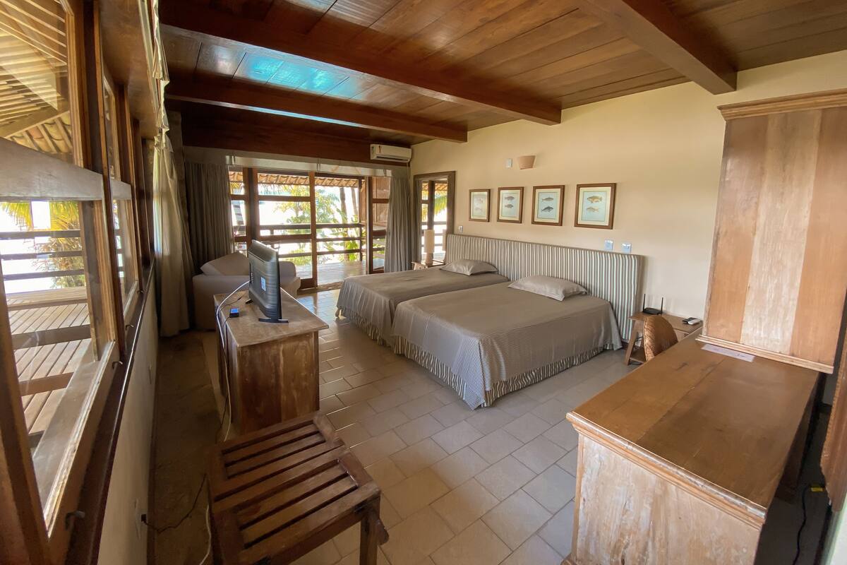 A room with two beds, a wooden desk, a TV, and large windows.