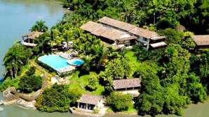 An aerial view of a resort with multiple buildings, a swimming pool, and lush greenery surrounding a body of water. - Santa Clara Hotel (Paraty)