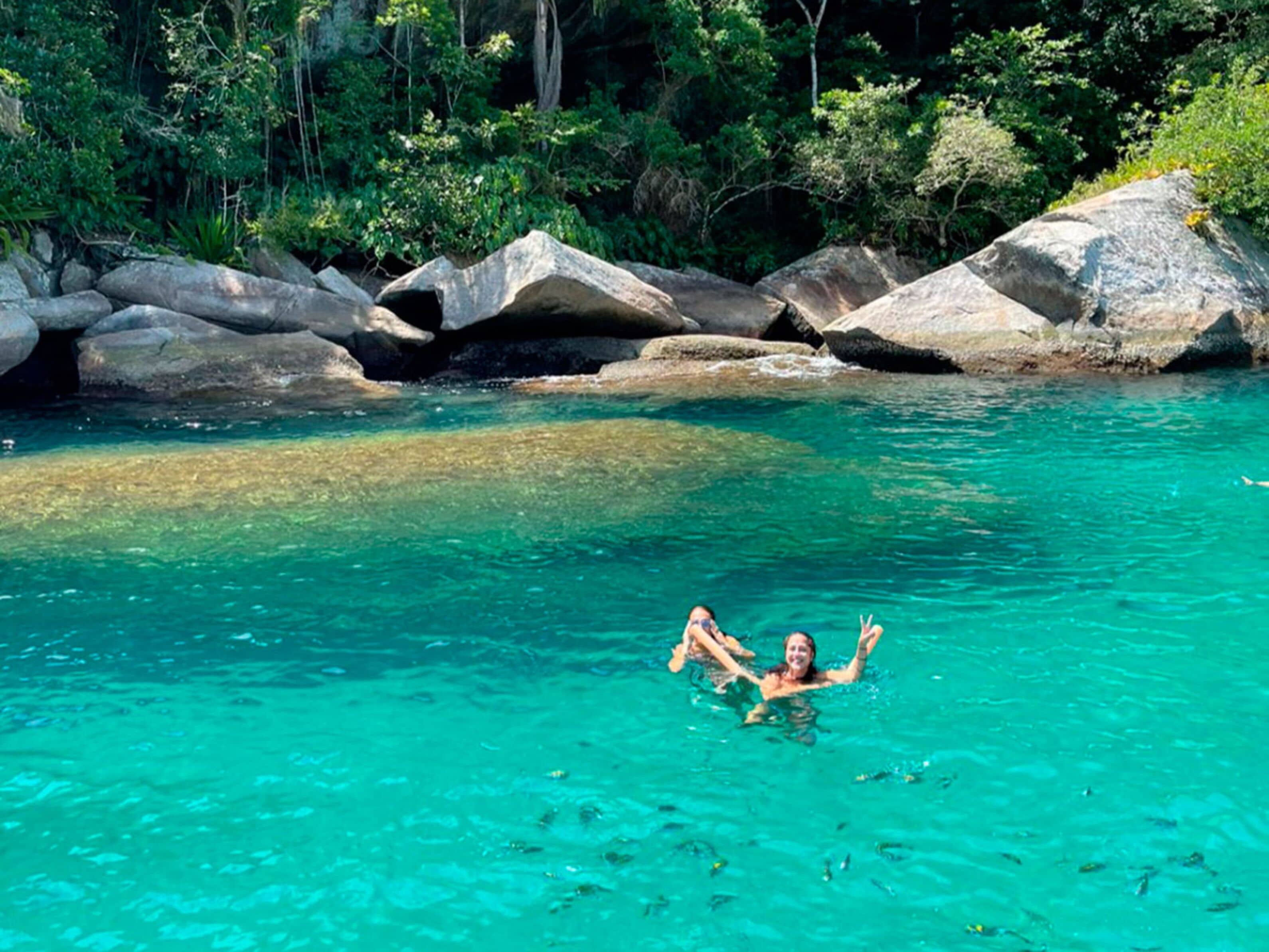 A person swimming in clear turquoise water surrounded by large rocks and dense greenery.