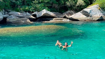 A person swimming in clear turquoise water surrounded by large rocks and dense greenery.