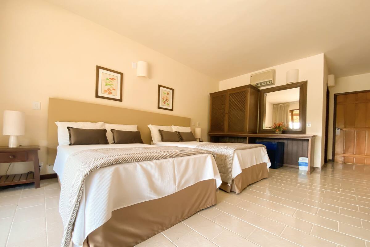 A hotel room with two beds, a desk, a mirror, and a wardrobe.