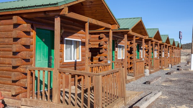 Une rangée de chalets en rondins, avec des portes vertes et des balustrades en bois.