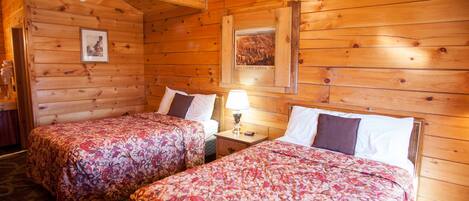 Ein Zimmer in einer Holzhütte mit zwei Betten, einem Nachttisch, einer Lampe und gerahmten Bildern an den Wänden.
