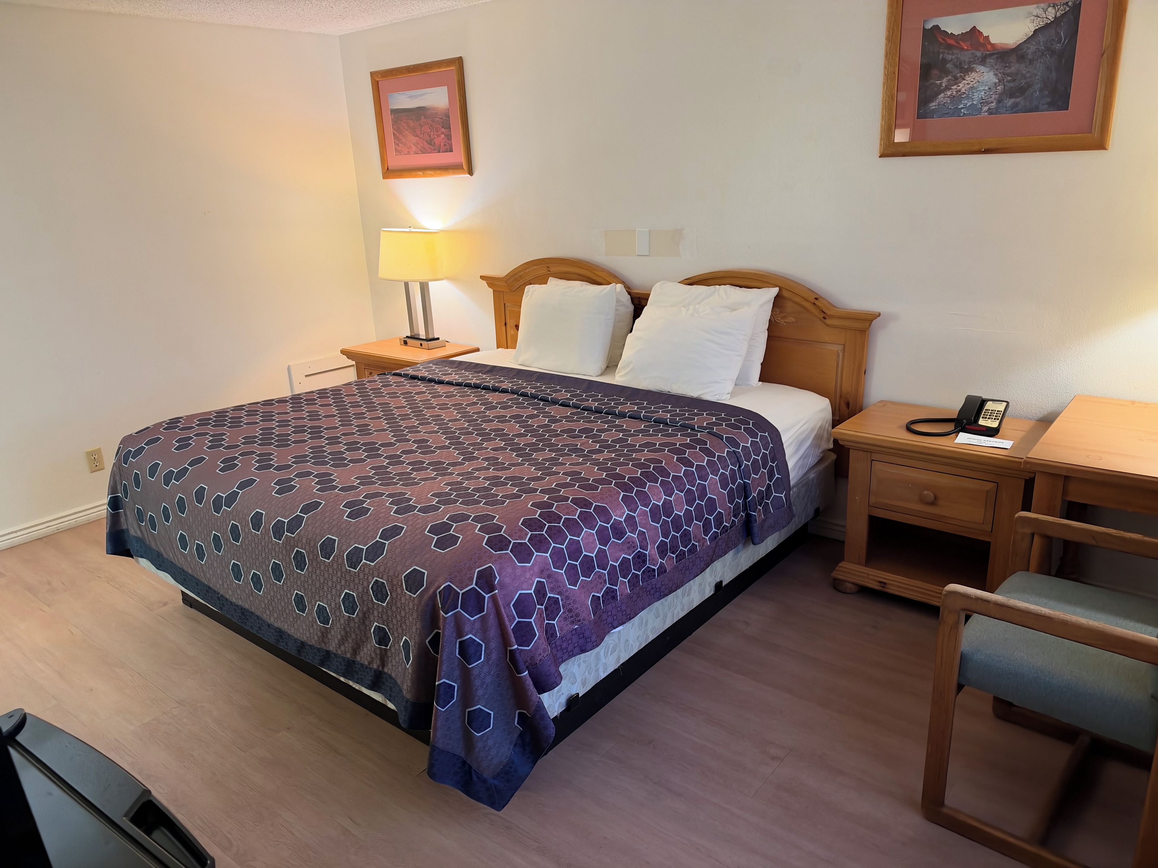 Una habitación de hotel con cama, mesita de noche, lámpara, silla y teléfono en la mesita.