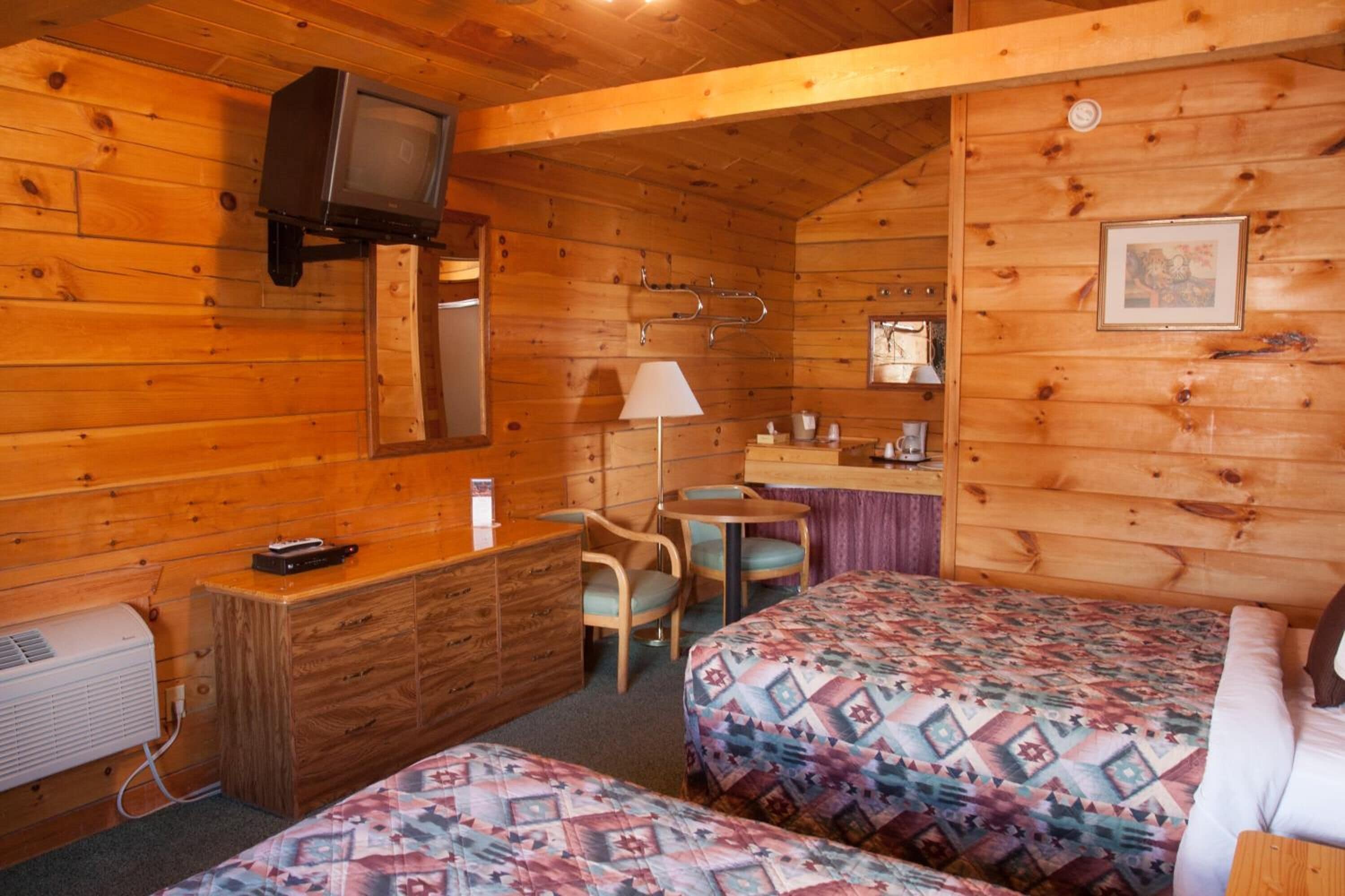 A cabin with two beds, a desk, a chair, a table, a TV, and a mirror.