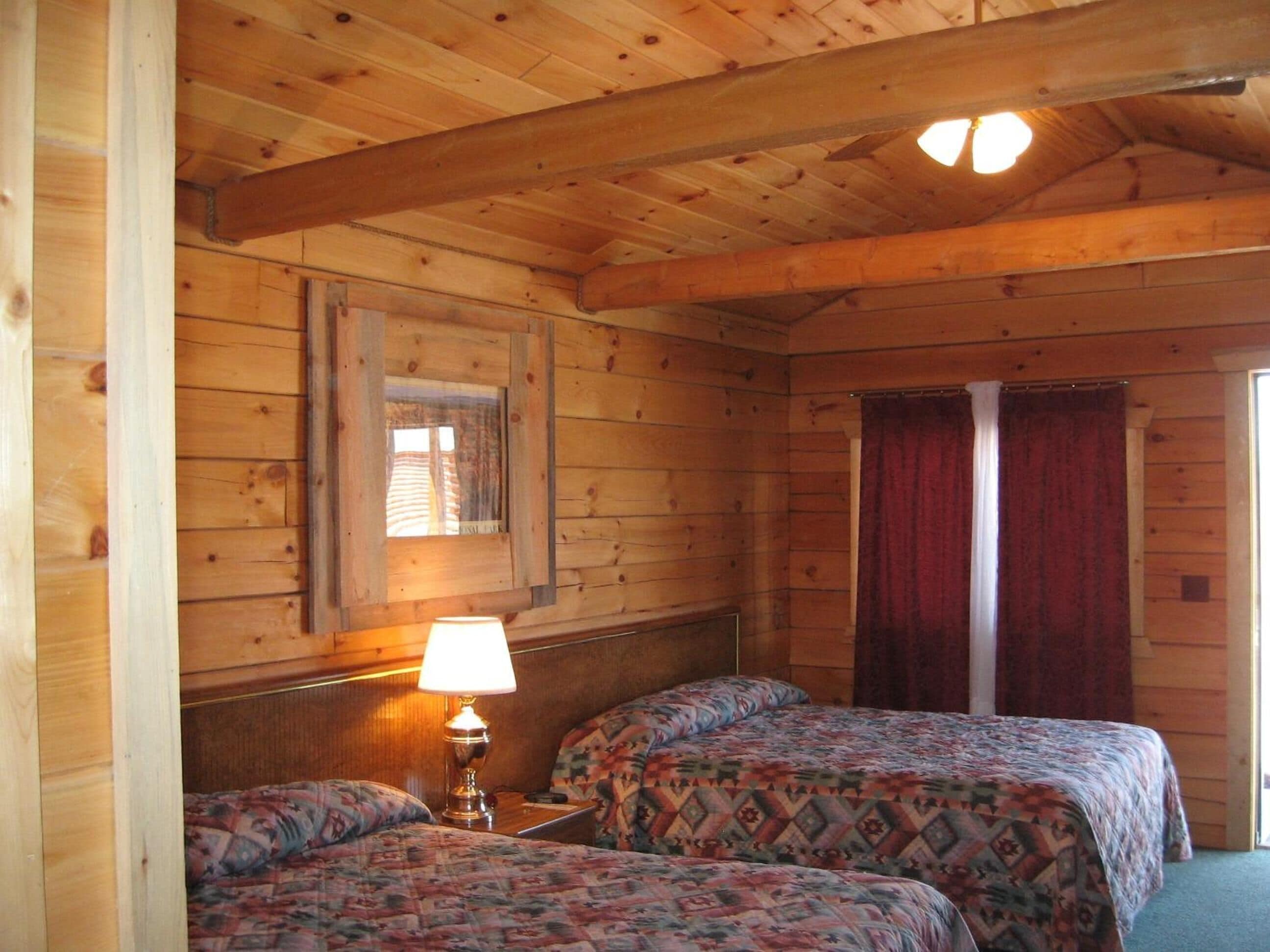 Habitación de cabaña de madera con dos camas, una lámpara, una ventana y una puerta.