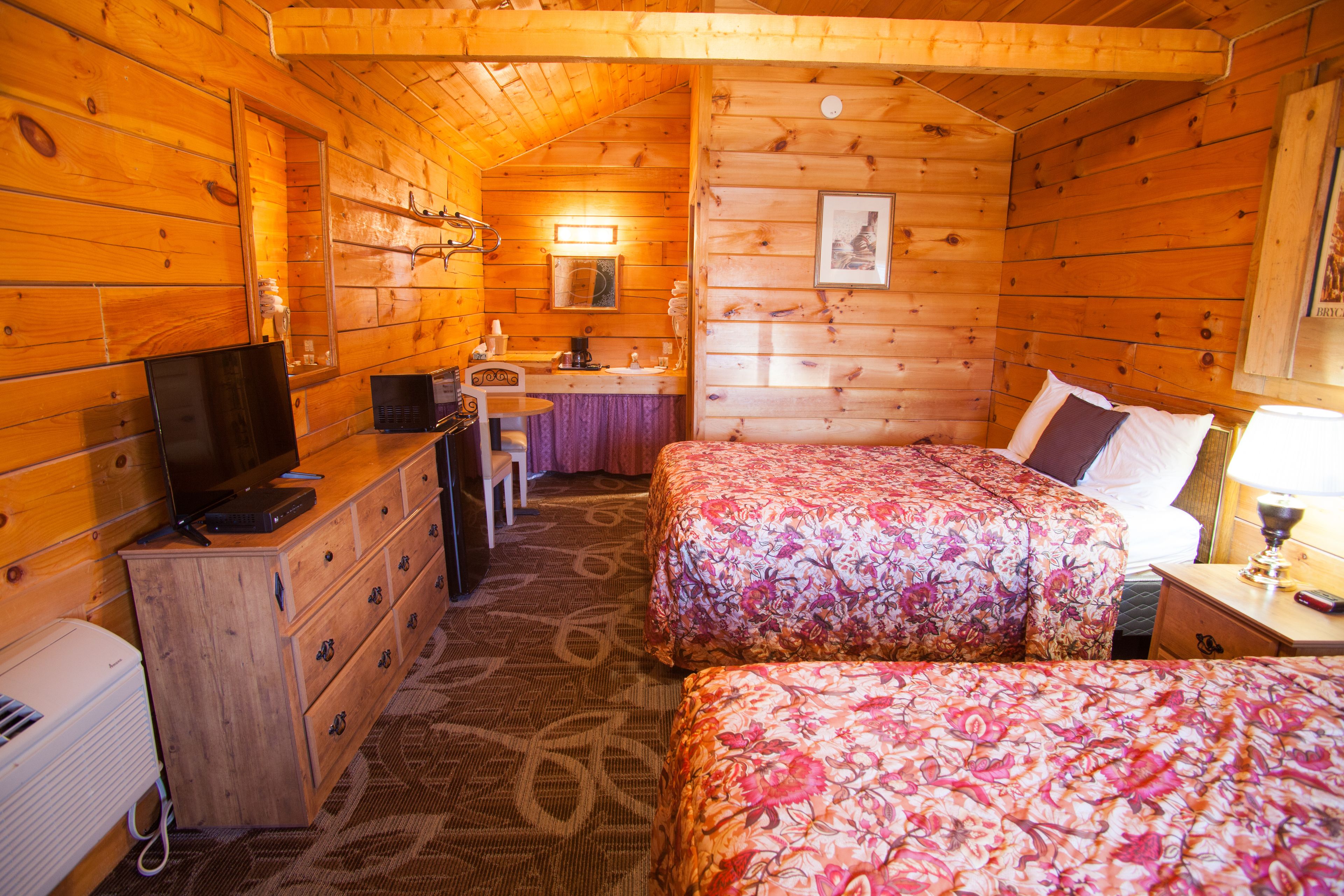A cabin-style room with two beds, a desk, a chair, a dresser, and a television.