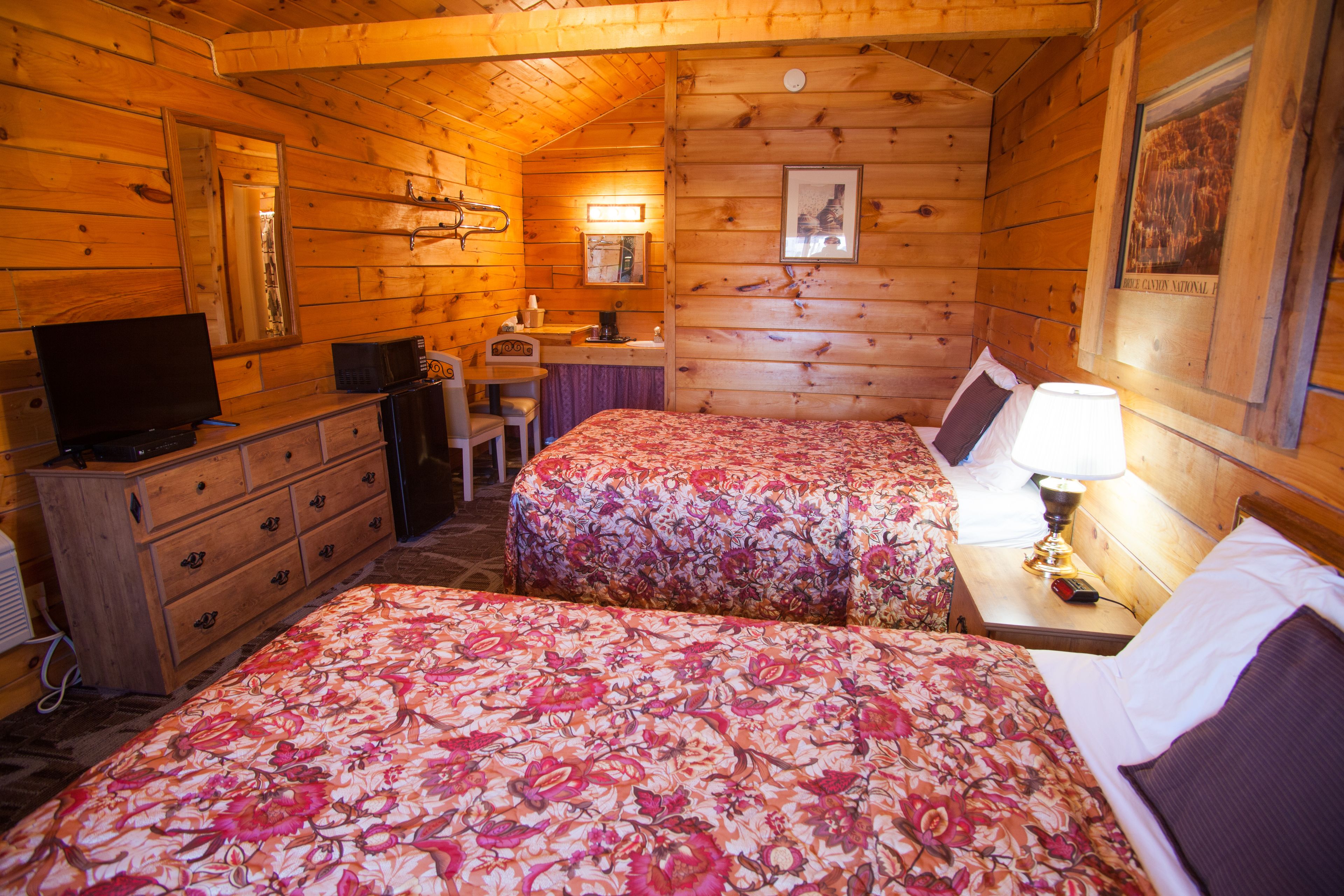 Ein Holzhütten-Zimmer mit zwei Betten, einem Schreibtisch, einem Stuhl, einem Fernseher und einem Spiegel.