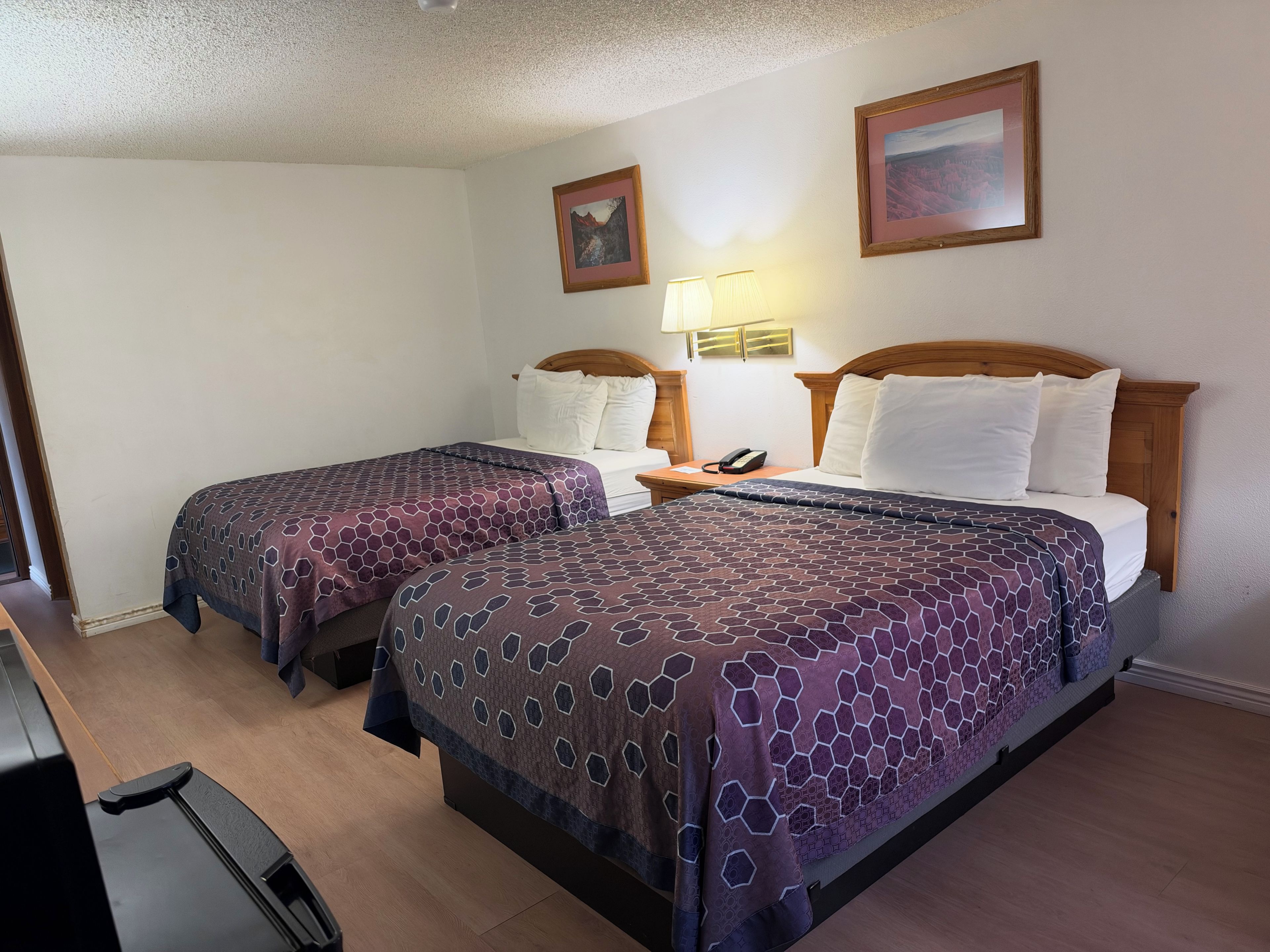 Habitación de hotel con dos camas, un escritorio, una silla, una lámpara y dos cuadros en la pared.