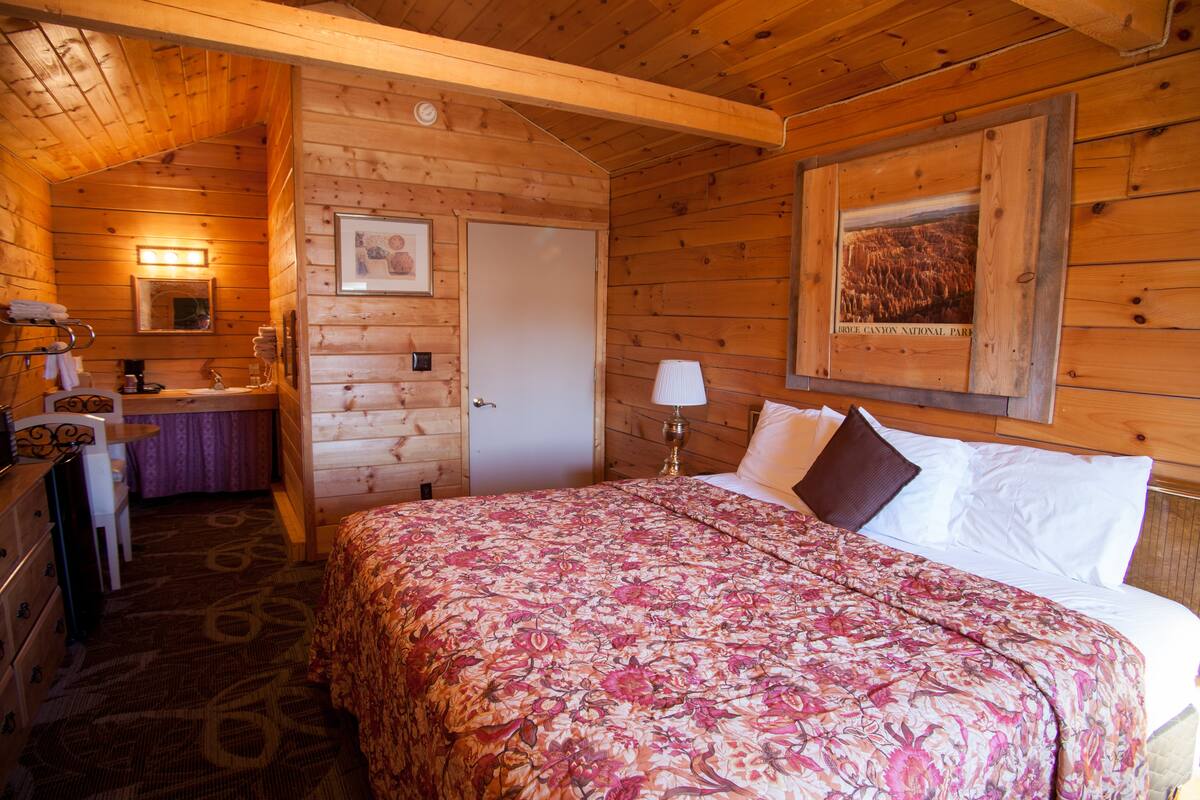 Quarto de cabana de madeira com cama, banheiro e escrivaninha.