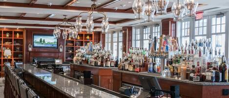 A bar area with a long counter, multiple bar stools, and a variety of bottles and glasses.