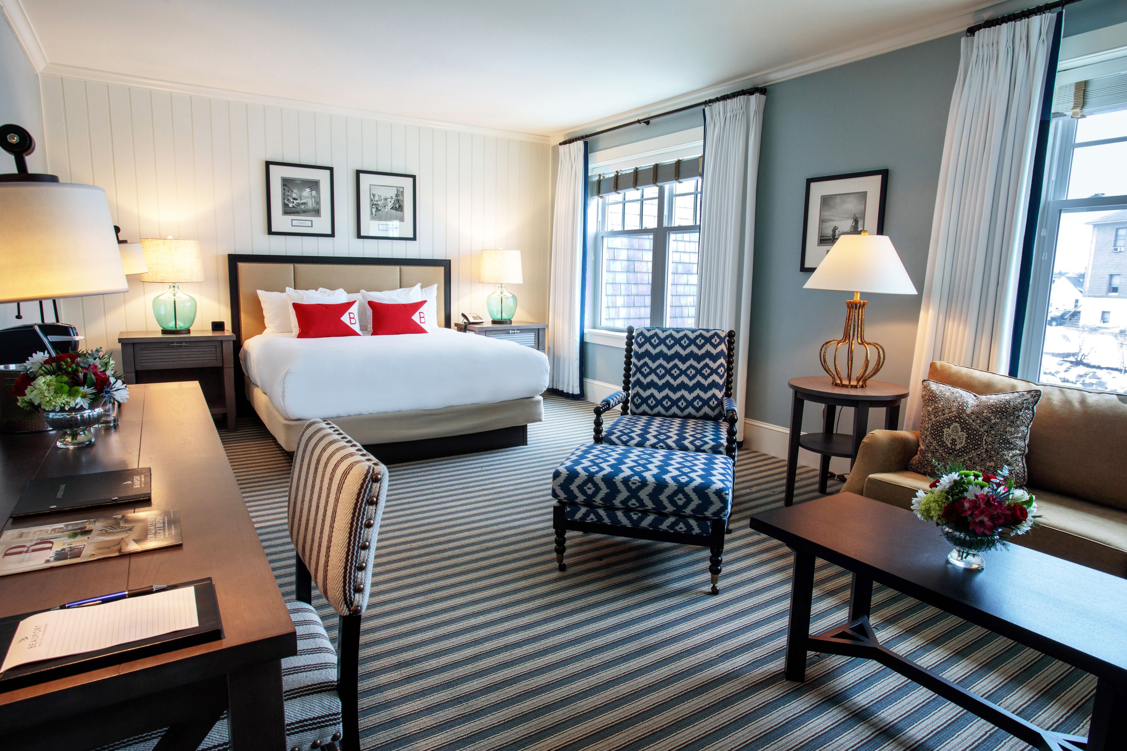 Quarto de hotel com uma cama grande, duas poltronas, um sofá, uma escrivaninha e uma janela com cortinas.