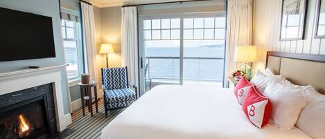 Habitación de hotel con una cama grande, chimenea, televisor y vista al mar.