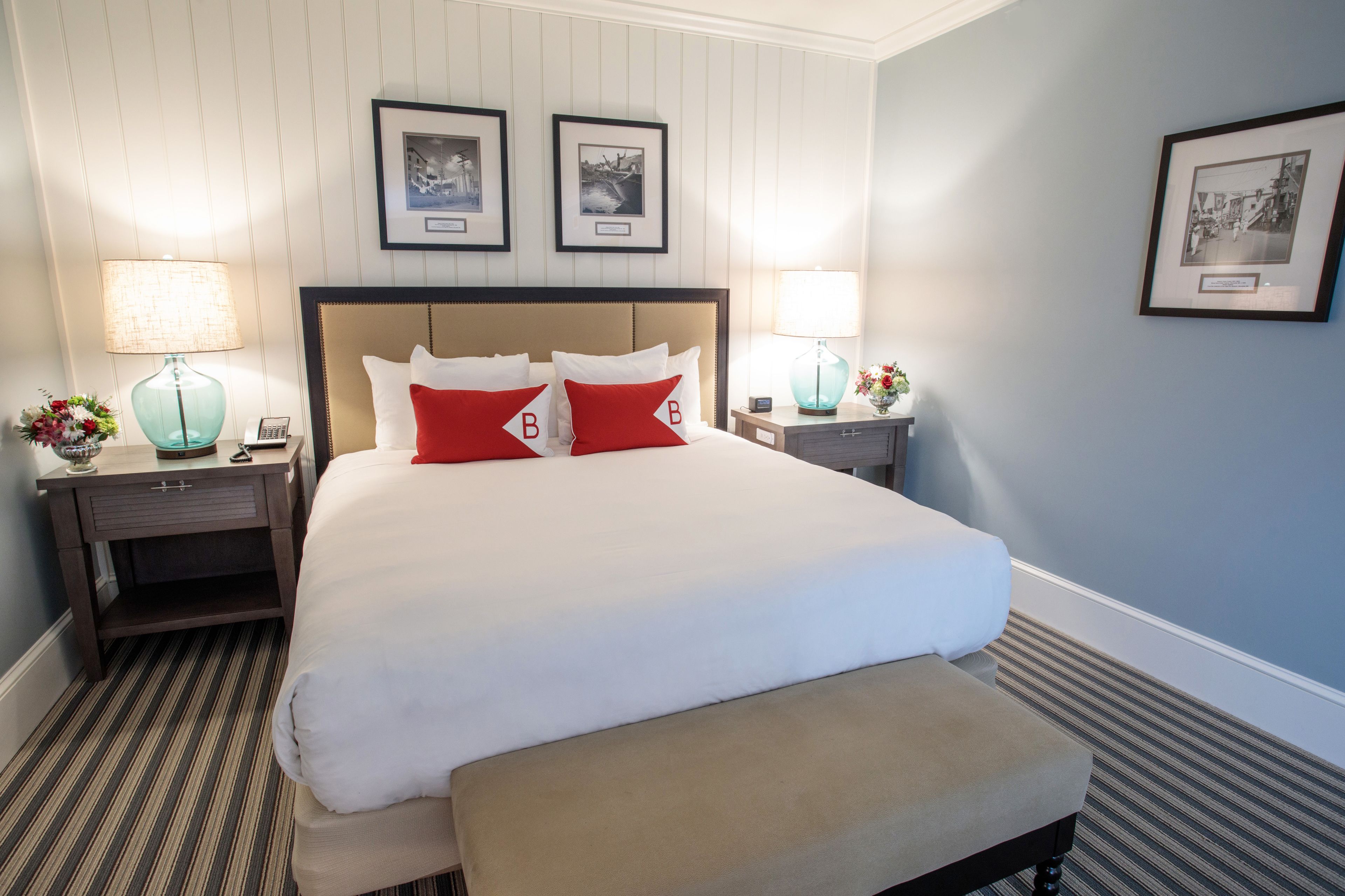 A hotel room with a large bed, two bedside tables with lamps, a bench, and framed pictures on the wall.