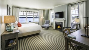 Una habitación de hotel con una cama grande, chimenea, televisor y vista al agua.
