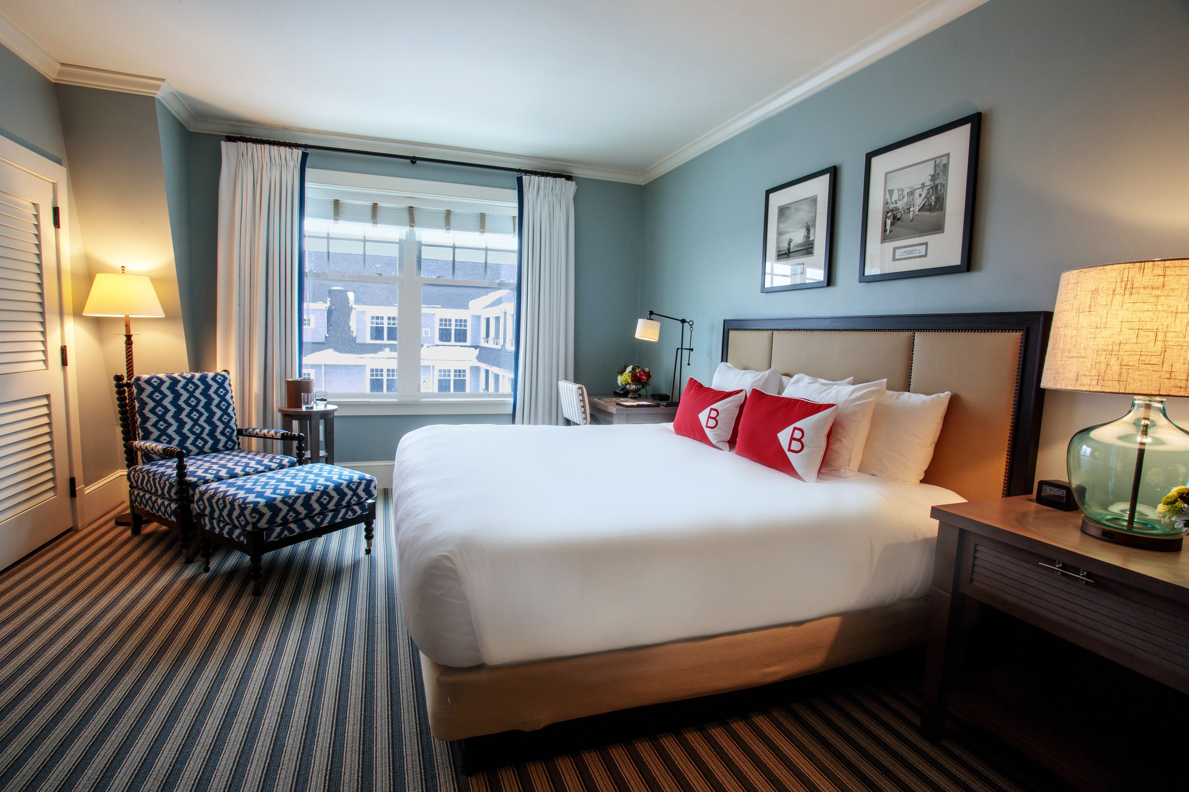 A hotel room with a large bed, a chair, a nightstand, a lamp, and a window with curtains.