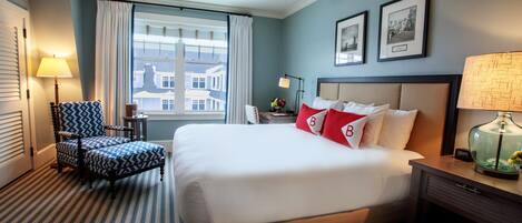 A hotel room with a large bed, a chair, a nightstand, a lamp, and a window with curtains.