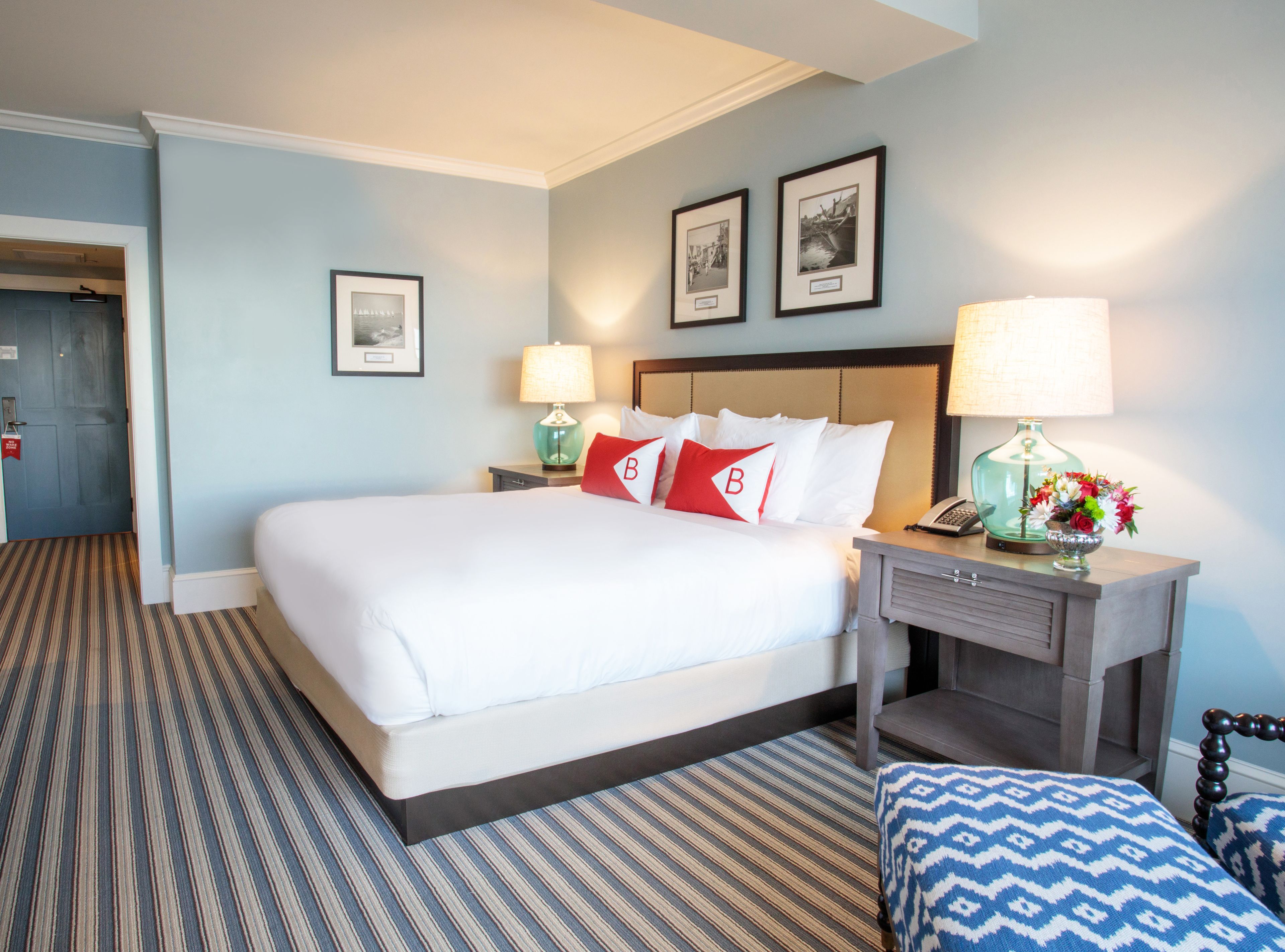 A hotel room with a large bed, two bedside tables, a nightstand, a chair, and a door.