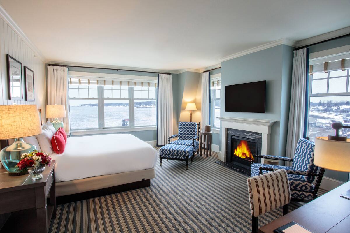 Habitación de hotel con una cama grande, chimenea, televisor y vista al agua.