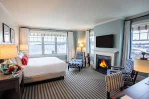 A hotel room with a large bed, a fireplace, a TV, and a view of the water.