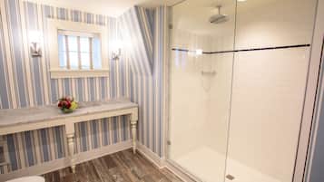 A bathroom with striped wallpaper, a marble countertop, a glass shower enclosure, and a wooden floor.