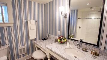 A bathroom with striped wallpaper, a marble sink, a large mirror, and a shower.