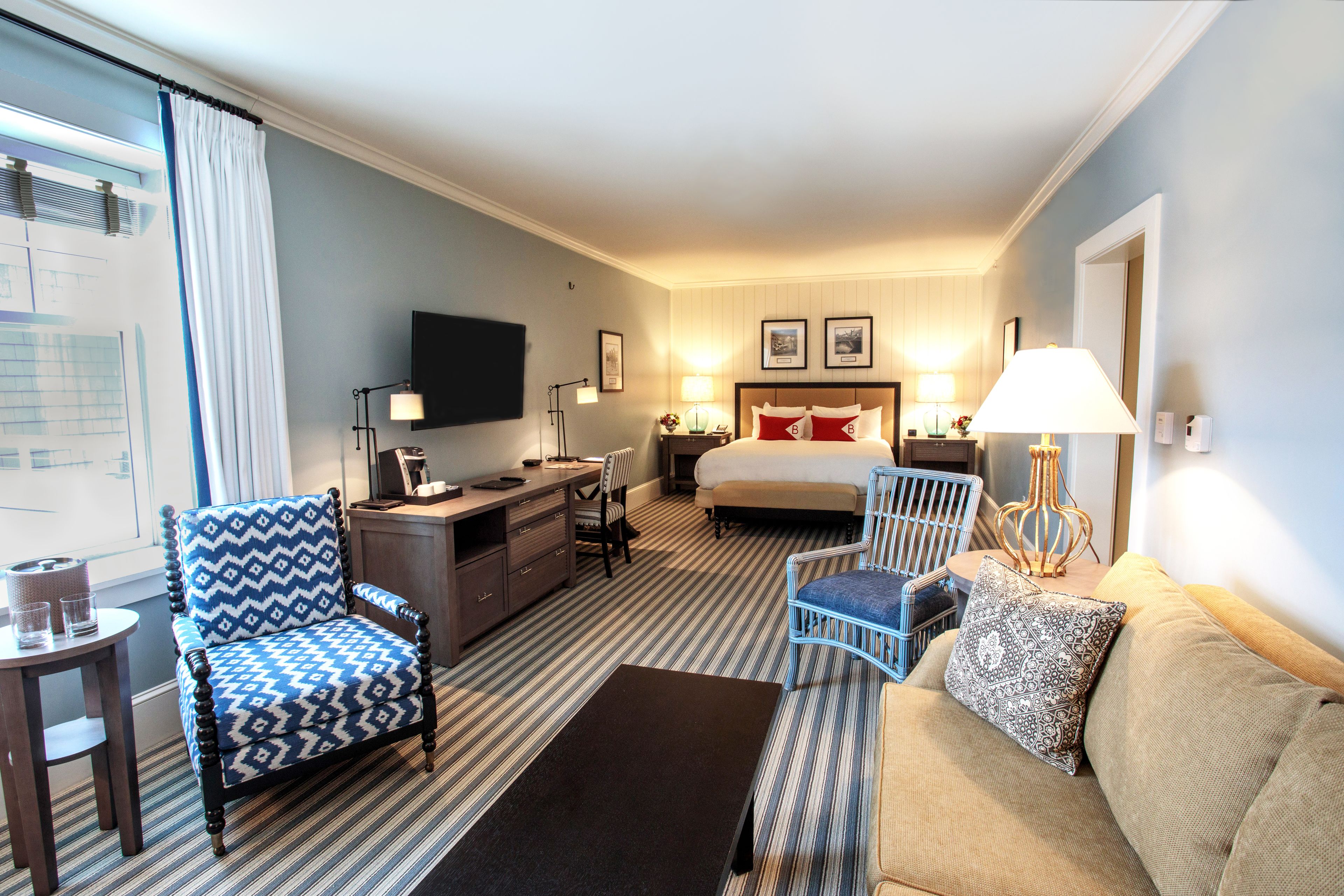 A hotel room with a bed, a desk, a chair, a sofa, and a TV.