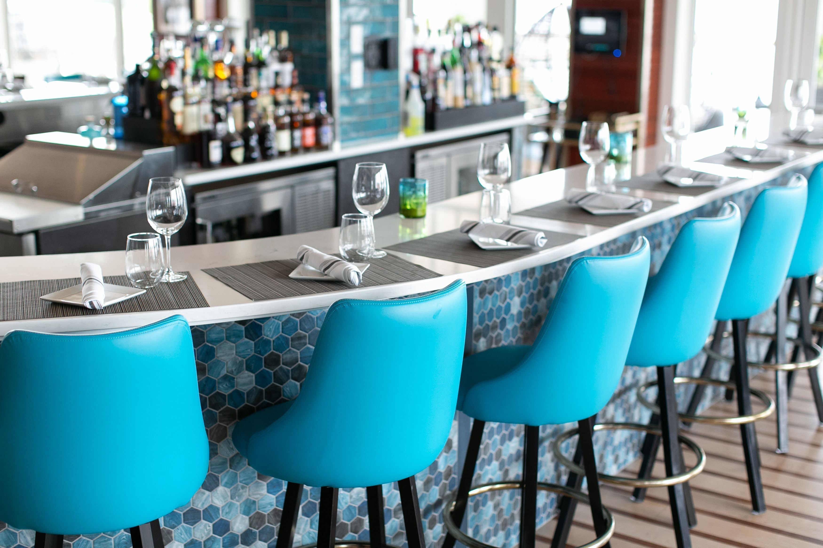 Un espace bar avec des chaises bleues, un long comptoir et une variété de bouteilles disposées en arrière-plan.