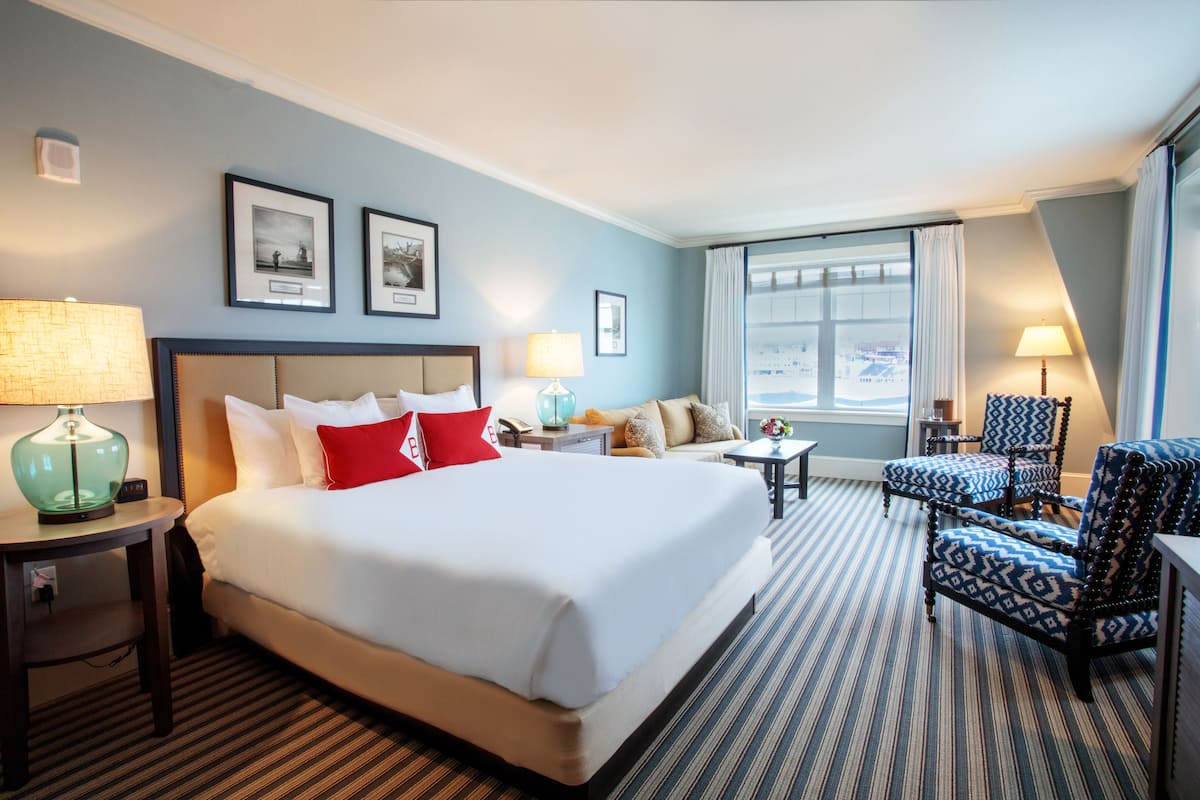 Una habitación de hotel con una cama grande, dos mesitas de noche, un sofá, una silla y una ventana con cortinas.