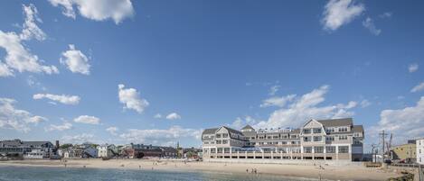 A beachfront hotel with multiple stories, a sandy beach, and clear blue skies.