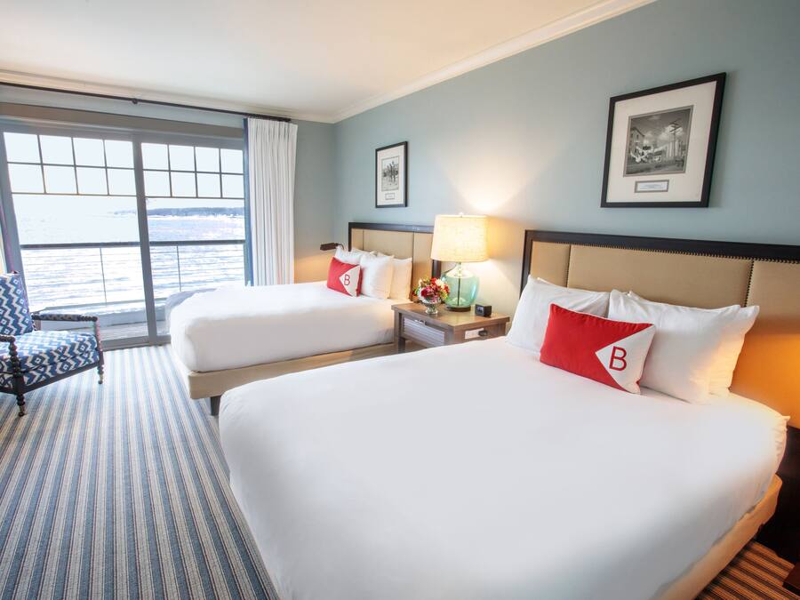 Habitación de hotel con dos camas, una silla, una mesita de noche y vista al mar.