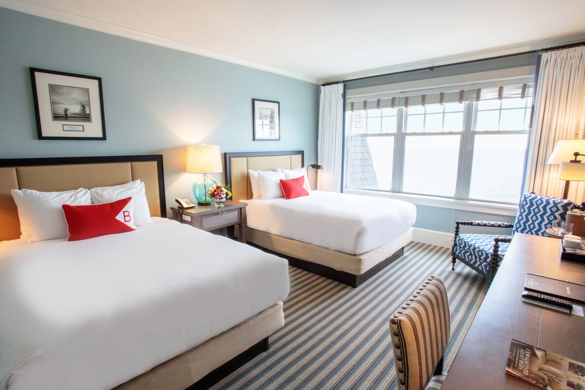 Habitación de hotel con dos camas, un escritorio y una ventana con cortinas.