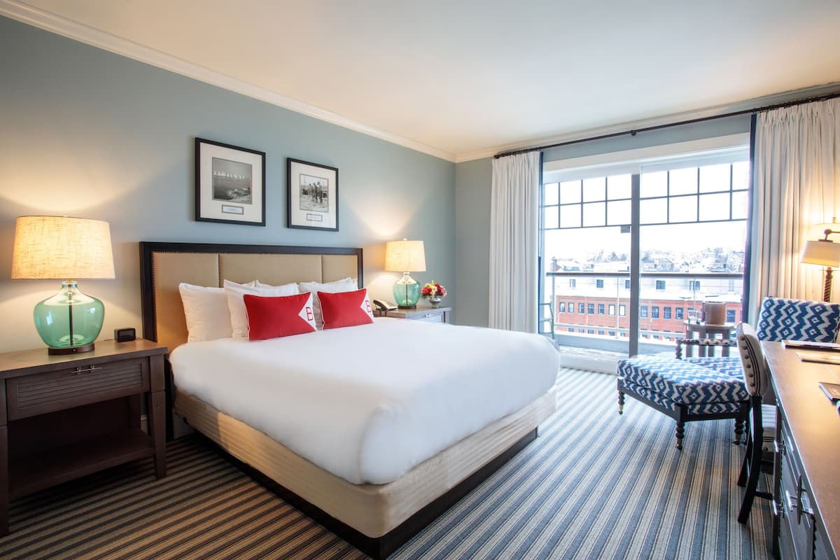 Una habitación de hotel con una cama grande, dos lámparas de noche, un escritorio con una silla y una ventana con cortinas.