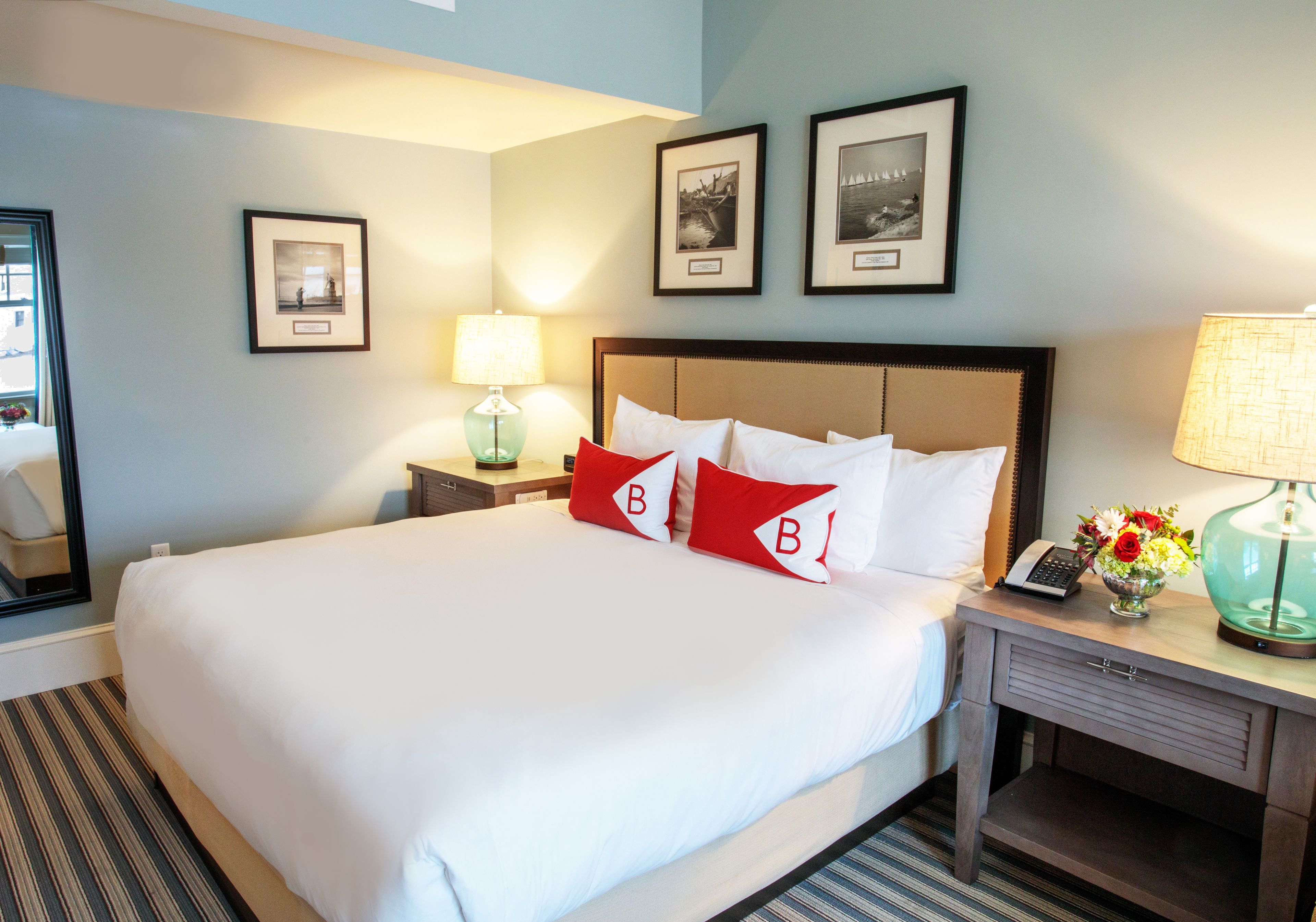 A hotel room with a large bed, two bedside tables, a nightstand, and a desk with a lamp. There are framed pictures on the wall.