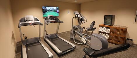 Une salle de sport équipée de tapis de course, d’un vélo elliptique et d’un banc de musculation.
