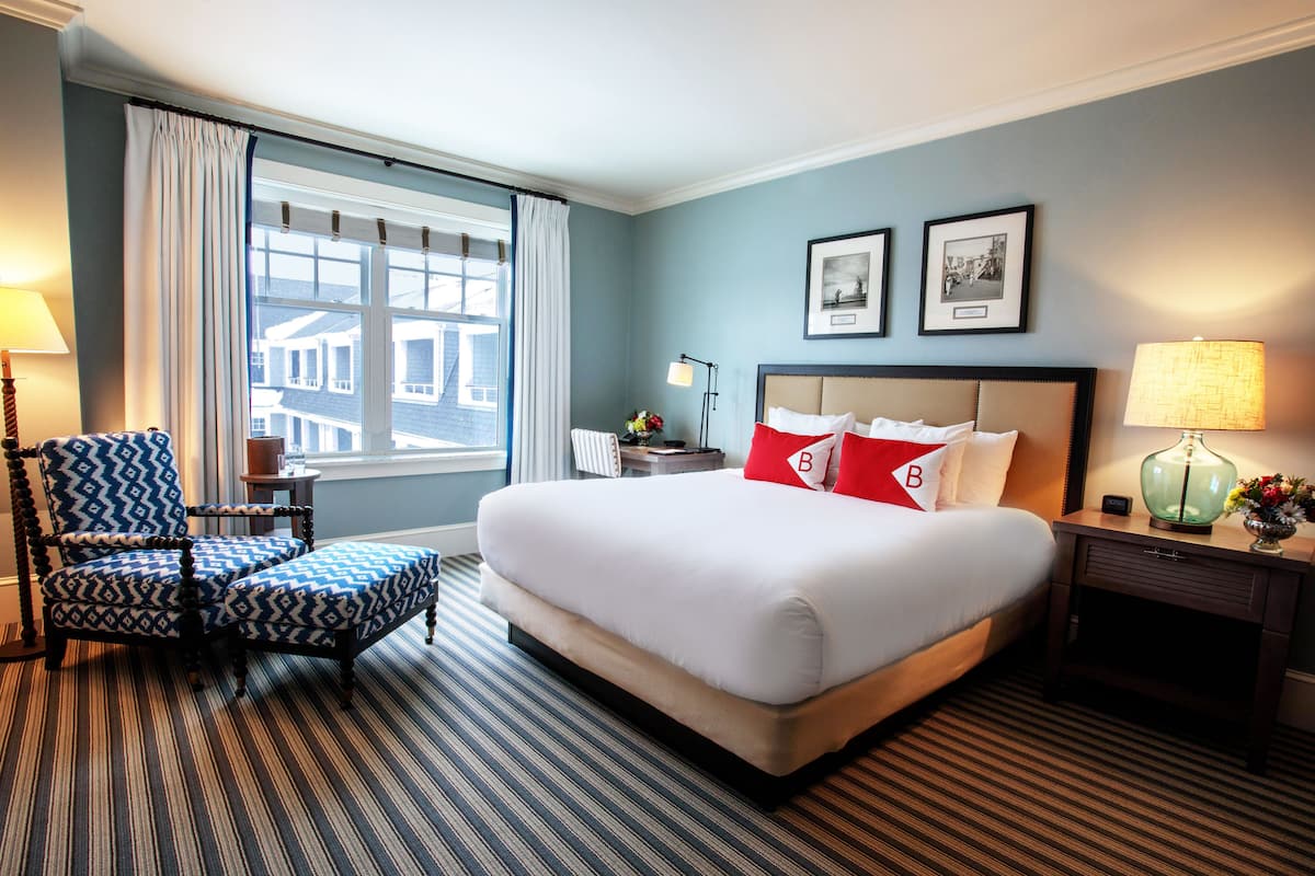 Una habitación de hotel con una cama grande, una silla, una mesita de noche y un ventanal con cortinas.