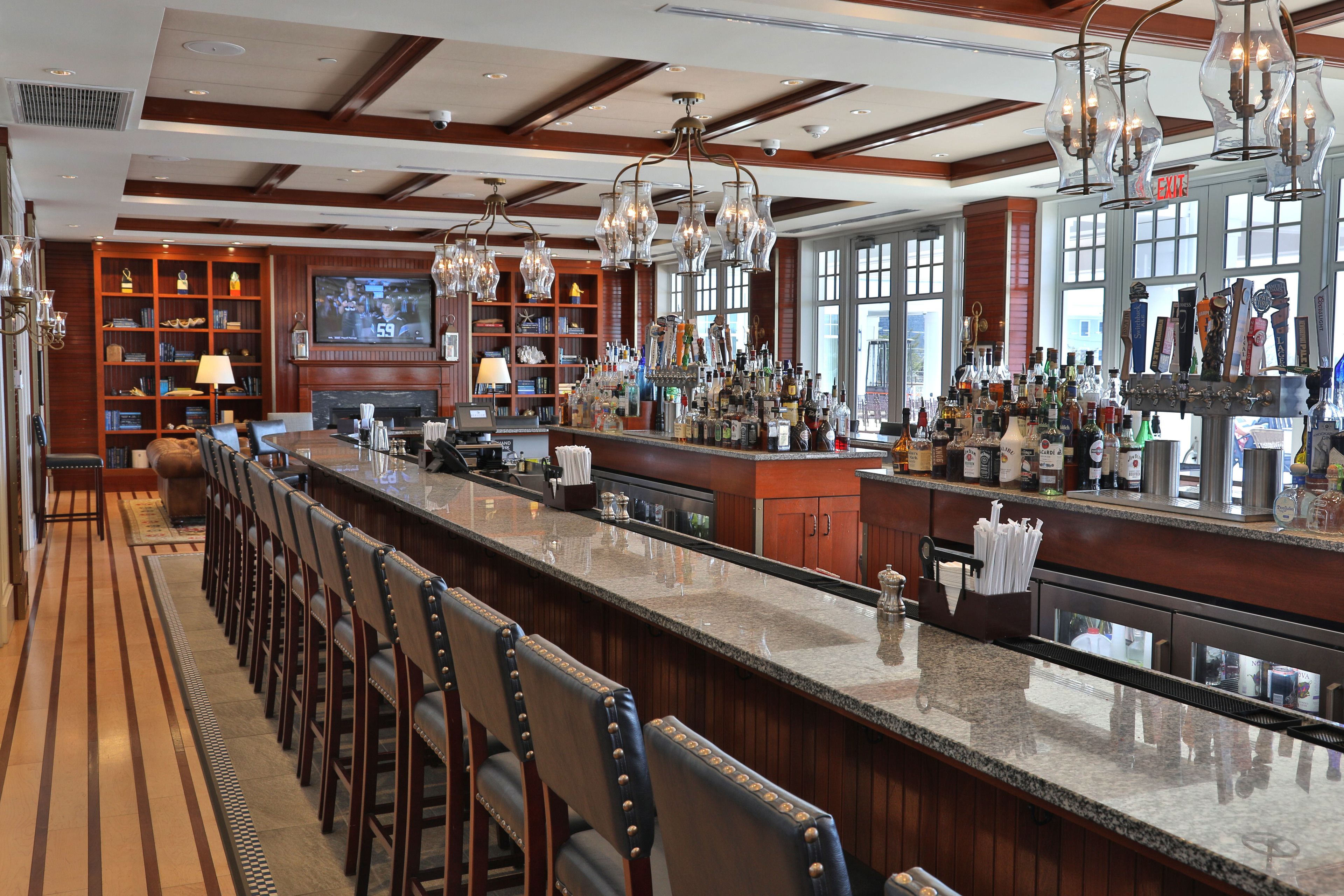 A bar area with a long counter, multiple bar stools, and a television screen displaying a sports game.