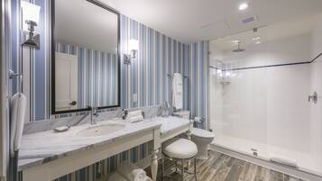A bathroom with striped wallpaper, a marble sink, a large mirror, a toilet, and a glass-enclosed shower.