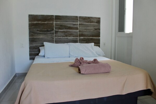 A neatly made bed with a beige bedspread and a pink towel, white pillows, and a wooden headboard. - Suite 24 ApartHotel By Xperience Hotels (Playa del Carmen)