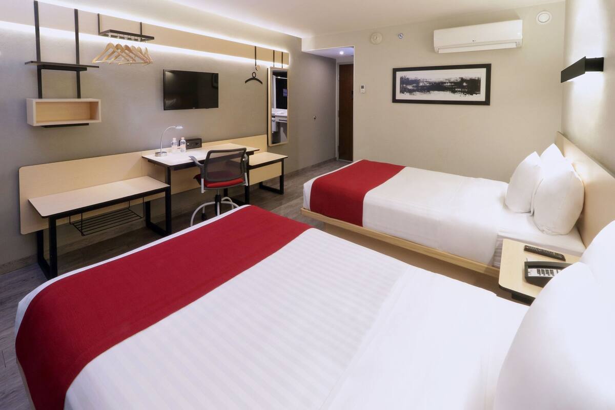 Een hotelkamer met twee bedden, een bureau, een stoel, een televisie en een spiegel.